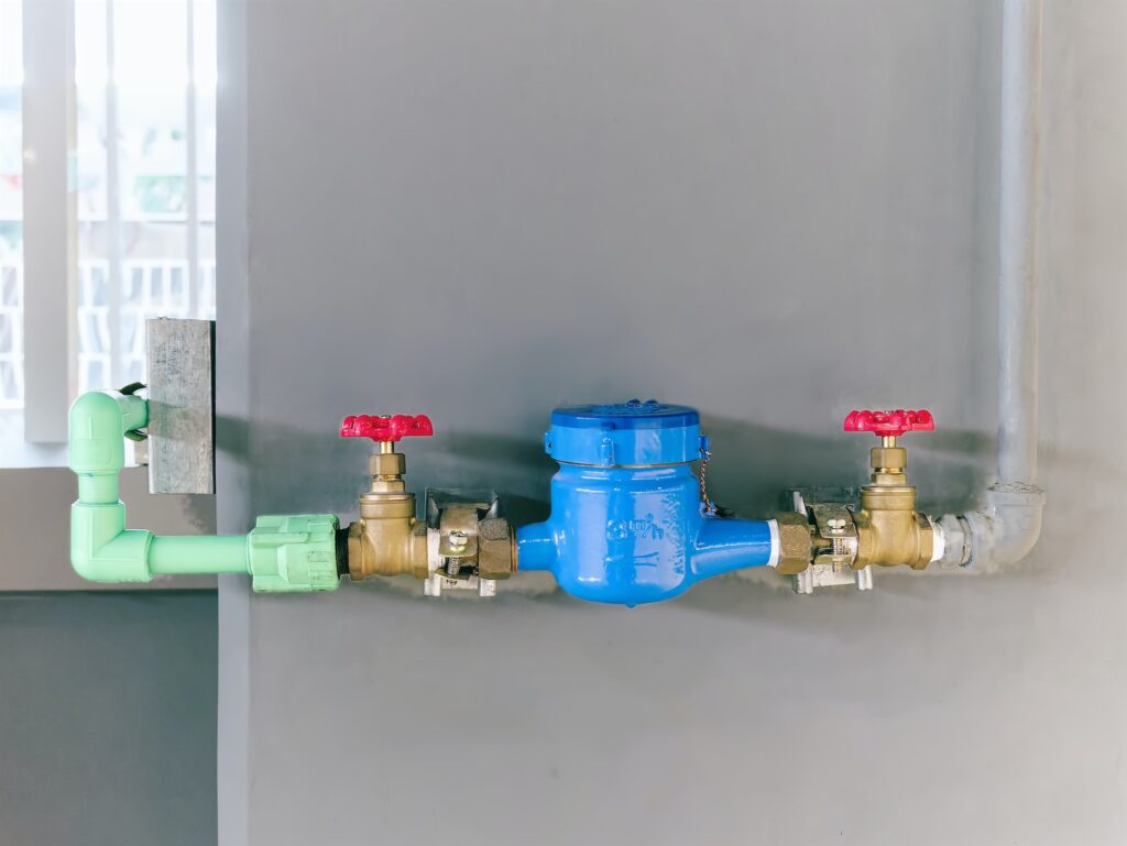 Water Pipeline with Valves and Meter Against Gray Wall